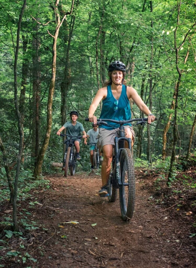 Family biking together on a scenic forest trail at Wildside Adventure Park in the Smoky Mountains.
