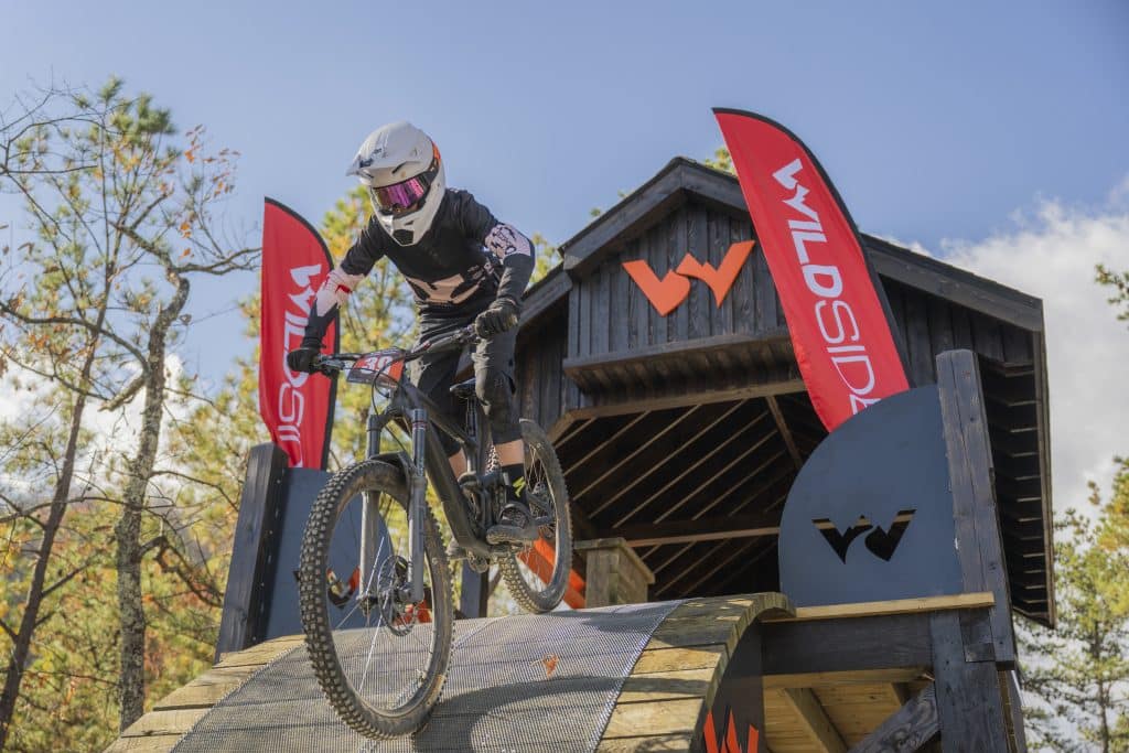 Mountain biker headed down ramp during a race with WildSide building behind him